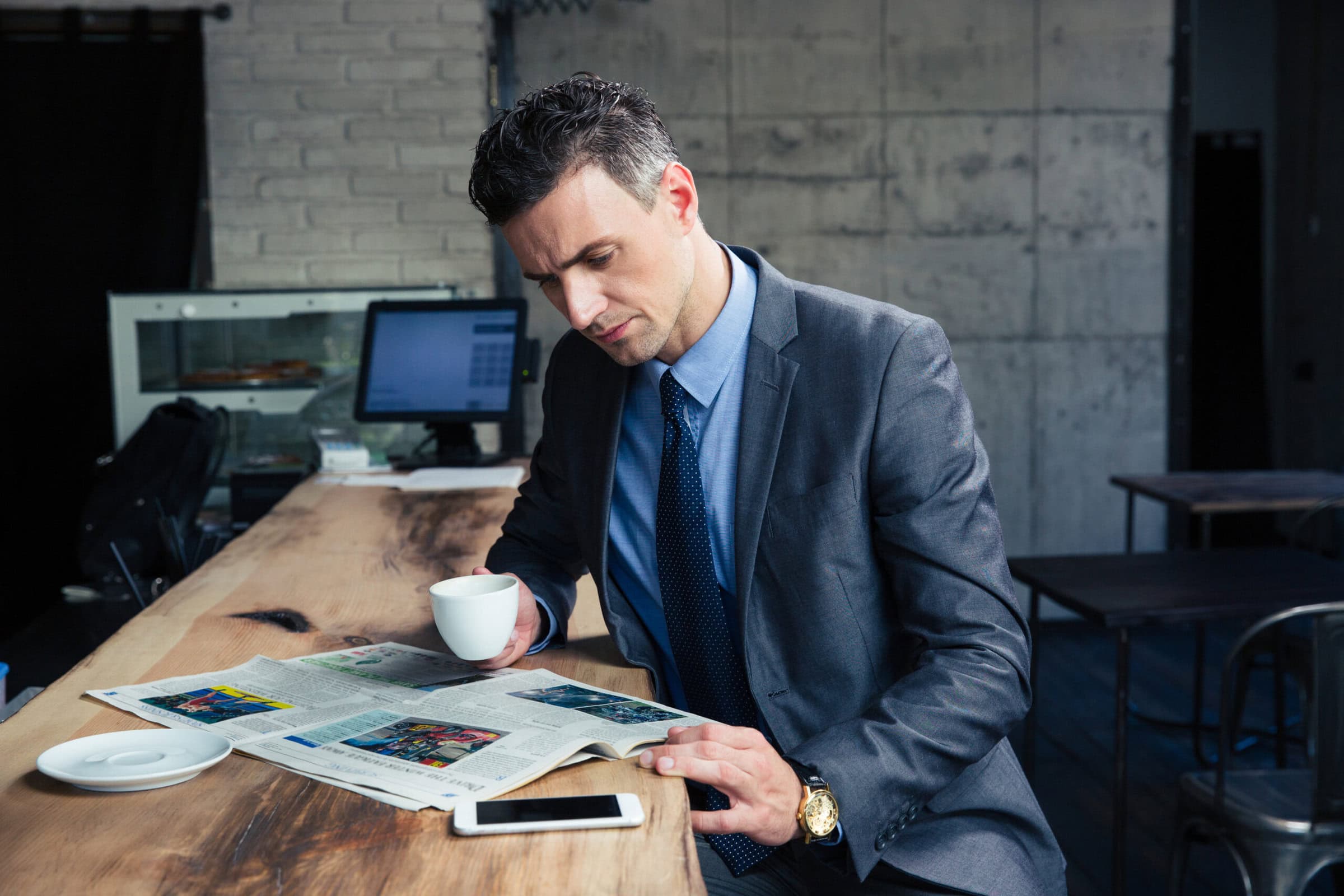 A man in a suit drinking coffee and reading news